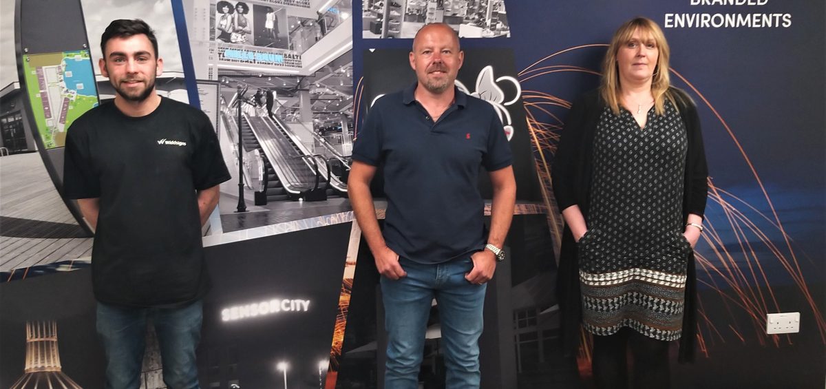 2 men and 1 women in front of coloured signage